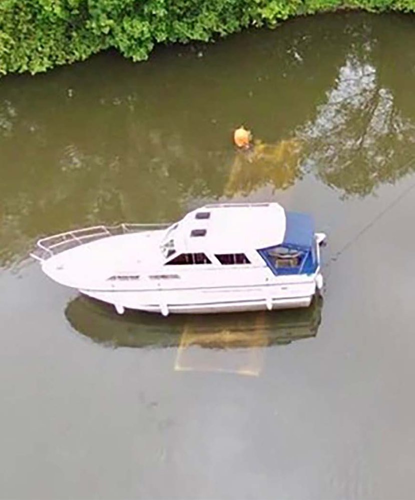 Luftaufnahme eines auf einem Wrack aufgelaufenen Motorboots in einem Fluss.