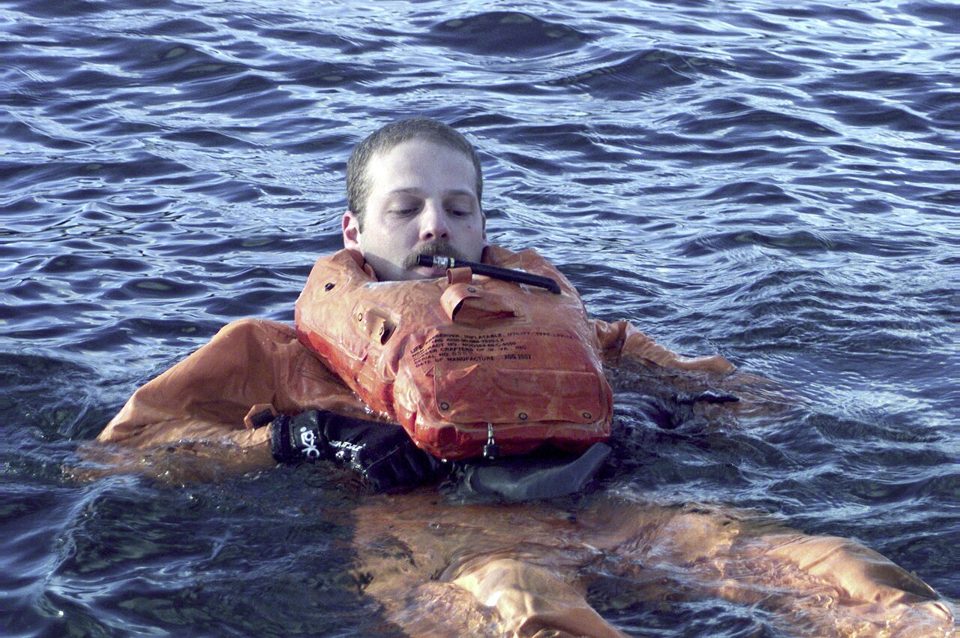 Ein Mann in Überlebensanzug und Weste schwimmt im kalten Wasser.
