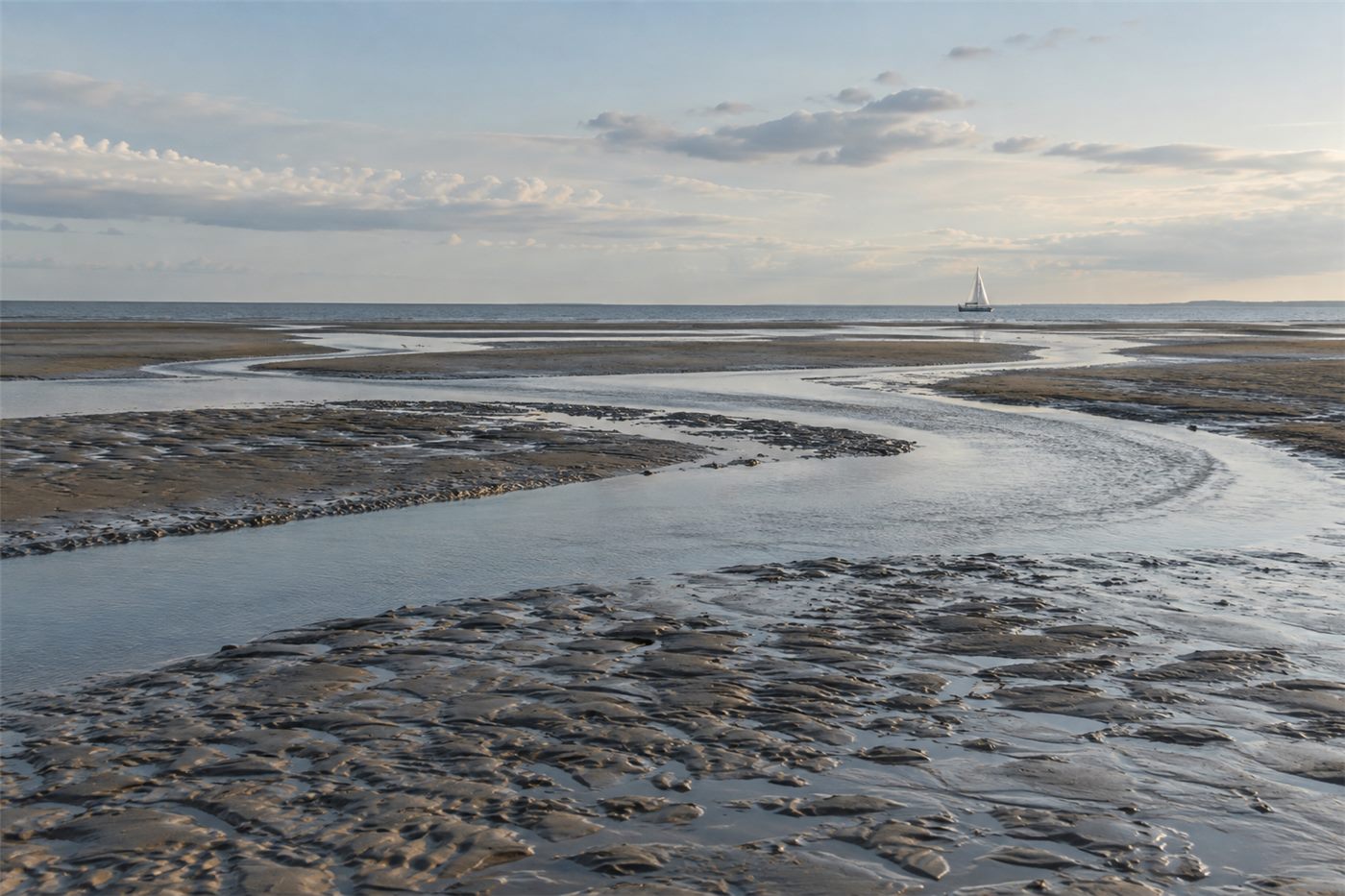 Wattenmeer – trockengefallene Wattflächen mit Prielen, Boot im Hintergrund.