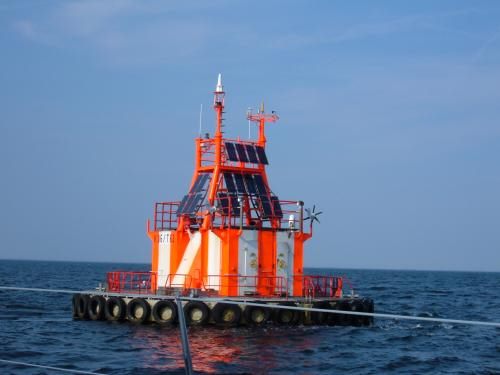 Foto: große rot-weiß gestreifte Tonne mit Solarmodulen, Laterne und Messgeräten in der Ostsee