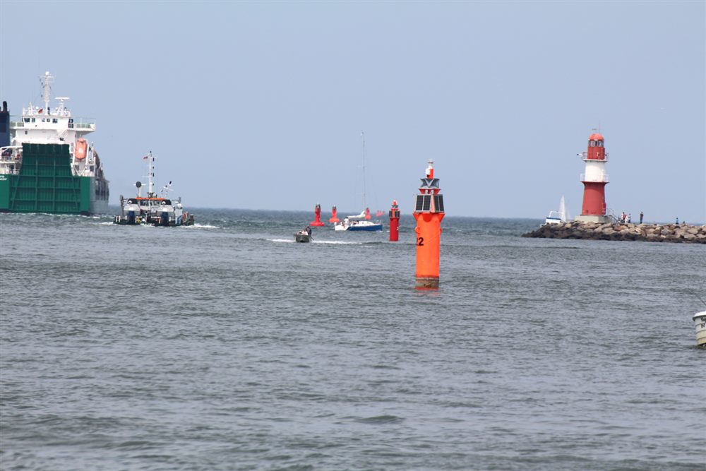 Foto: Hafeneinfahrt mit roten Leuchttonnen, auslaufenden Schiffen und rot-weißem Molenfeuerturm